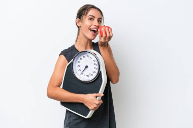 Genç, güzel Uruguaylı bir kadın beyaz arka planda, tartı makinesi ve elma ile izole edilmiş.