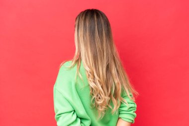 Genç Uruguaylı kadın kırmızı arka planda izole edilmiş ve arkasına bakıyor.