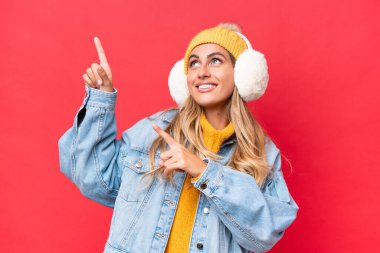 Kırmızı arka planda izole edilmiş kışlık kuklalar takan genç ve güzel Uruguaylı kadın işaret parmağıyla işaret ediyor. Harika bir fikir.