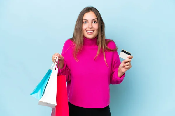 Ung Vacker Kvinna Isolerad Blå Bakgrund Håller Shoppingväskor Och Förvånad — Stockfoto