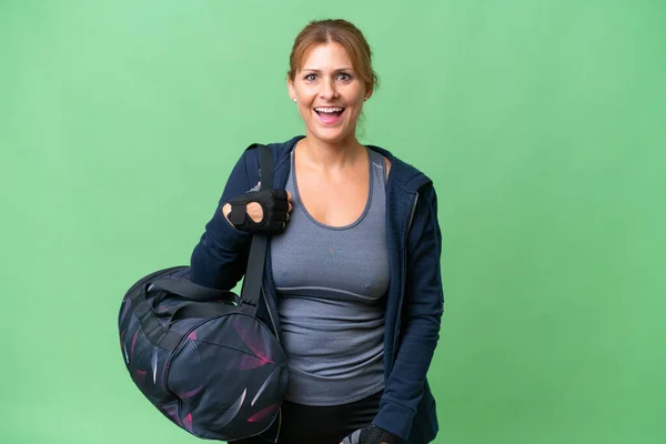 Middle-aged sport woman with sport bag over isolated background with surprise facial expression