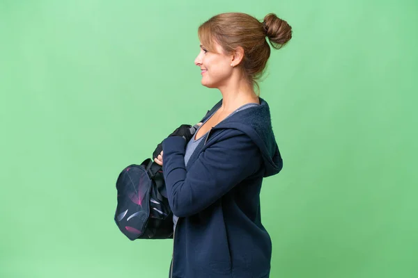 Middle-aged sport woman with sport bag over isolated background in lateral position