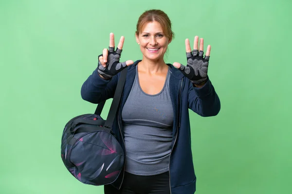 Middle-aged sport woman with sport bag over isolated background counting eight with fingers