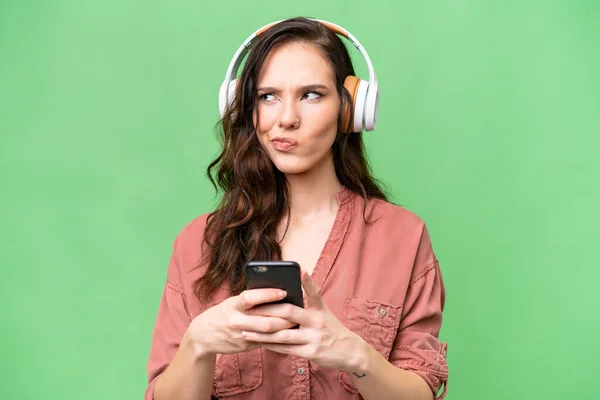 Giovane Donna Caucasica Sfondo Isolato Ascoltare Musica Con Cellulare Pensare — Foto Stock