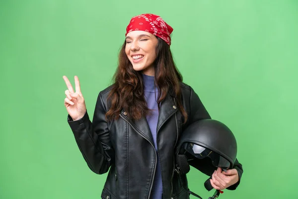 若いですCaucasian女性とともにオートバイヘルメット上の隔離された背景笑顔とショー勝利サイン — ストック写真