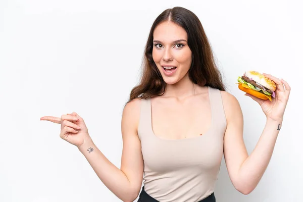 Young Caucasian Woman Holding Burger Isolated White Background Surprised Pointing — Stock Photo, Image