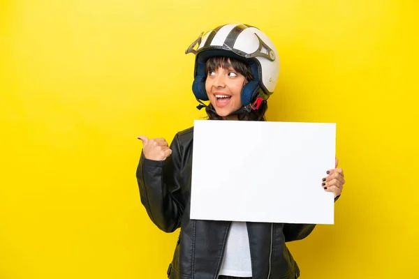 stock image Young latin woman with a motorcycle helmet isolated on yellow background holding an empty placard and pointing side