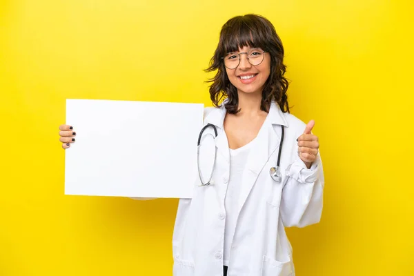 年轻的医生拉汀女士 被隔离在黄色背景下 手里拿着一个空布告 大拇指高举 — 图库照片