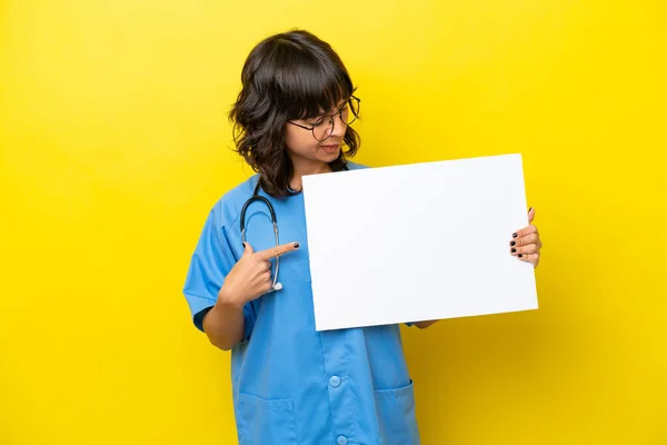 年轻的护士医生女士 黄底孤零零地举着一张空空的标语牌 满脸喜色 指点着它 — 图库照片