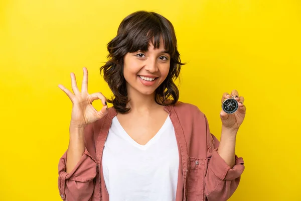 stock image Young latin woman holding compass isolated on yellow background showing ok sign with fingers