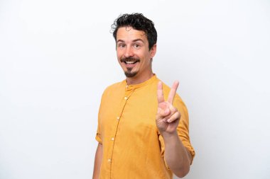 Bıyıklı genç adam beyaz arka planda izole edilmiş gülümsüyor ve zafer işareti gösteriyor.