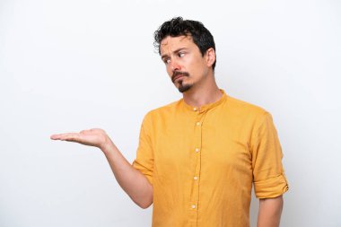 Bıyıklı genç adam beyaz arka planda izole edilmiş. Kopyalama alanını şüphe ile tutuyor.