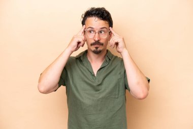 Beyazlı genç bir adam bej arka planda izole edilmiş. Şüpheleri ve düşünceleri var.