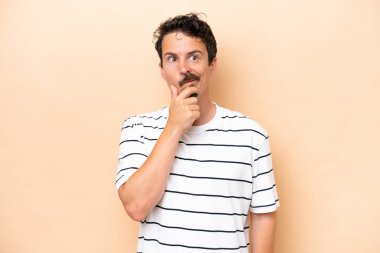 Beyazlı genç bir adam bej arka planda izole edilmiş. Şüpheleri ve düşünceleri var.