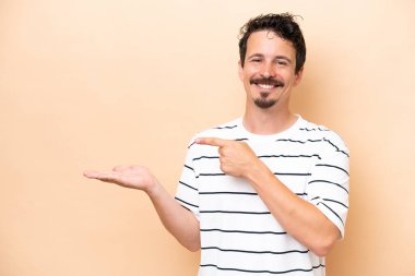 Beyazlı genç bir adam bej arka planda izole edilmiş. Elinde bir ilan vermek için avuç içi hayali fotokopi makinesi var.