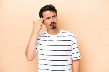 Genç beyaz adam bej arka planda izole edilmiş ve intihar jesti yapmada sorun yaşıyor.