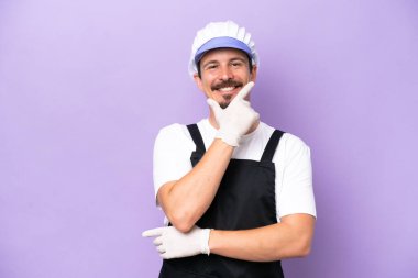Mor arka planda izole edilmiş önlük giyen balıkçı adam mutlu ve gülümsüyor.