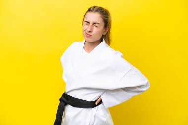 Karate yapan beyaz bir kadın, sarı arka planda izole edilmiş, gayret gösterdiği için sırt ağrısı çekiyor.