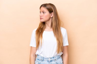 Beyazlı genç bir kadın bej arka planda izole edilmiş, yan tarafa bakıyor.