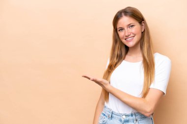 Beyazlı genç bir kadın bej arka planda izole edilmiş bir şekilde bir fikir sunuyor ve gülümsüyor.