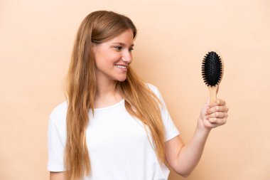 Saçları taranmış, bej arka planda mutlu bir yüzü olan genç, güzel sarışın kadın.