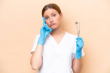 Beyaz dişçi kadının elinde bej arka planda izole edilmiş aletler var.