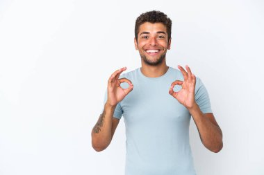 Beyaz arka planda izole edilmiş yakışıklı Brezilyalı bir adam iki eliyle tamam işareti gösteriyor.