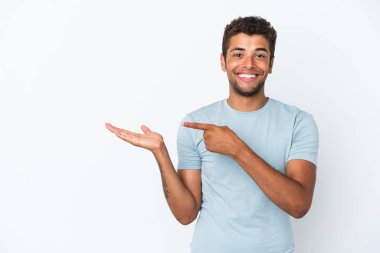 Beyaz arka planda izole edilmiş yakışıklı Brezilyalı bir adam bir ilan vermek için avuç içi hayali bir şey tutuyor.