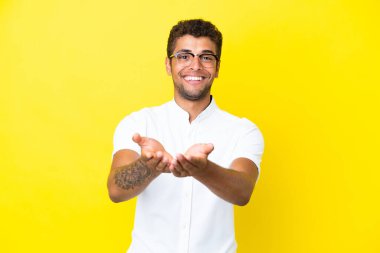 Sarı arka planda izole edilmiş yakışıklı Brezilyalı bir adam. Avucunun içinde bir ilan vermek için hayali bir mekan tutuyor.