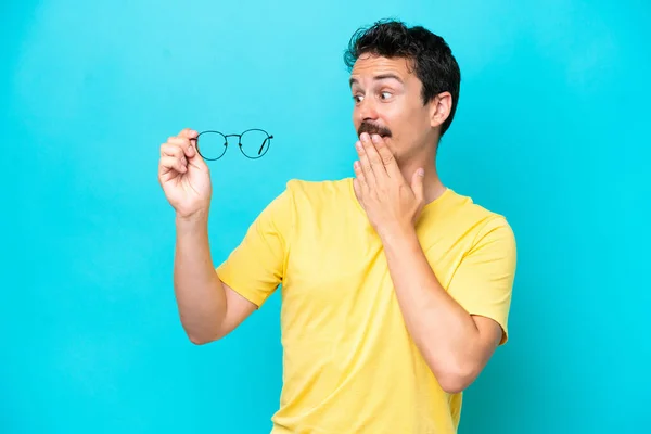 Giovane Uomo Caucasico Che Tiene Gli Occhiali Isolati Sfondo Blu — Foto Stock