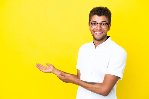 stock image Young handsome Brazilian man isolated on yellow background extending hands to the side for inviting to come