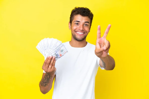 Jonge Braziliaanse Man Neemt Veel Geld Geïsoleerd Gele Achtergrond Glimlachend — Stockfoto