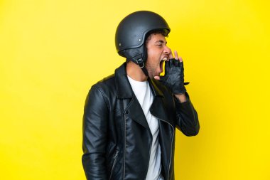 Sarı arka planda izole edilmiş motosiklet kasklı genç Brezilyalı adam ağzı sonuna kadar açık bağırıyor.