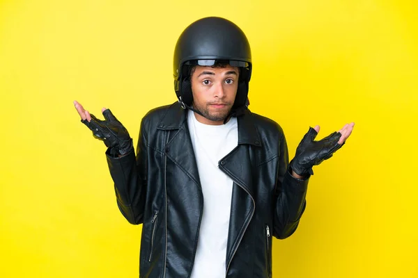 若いですブラジル人男とともにオートバイヘルメット隔離上の黄色の背景疑問を持ちながら手を上げる — ストック写真