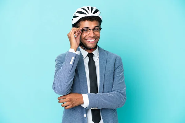 Young business Brazilian man with bike helmet isolated on blue background with glasses and happy