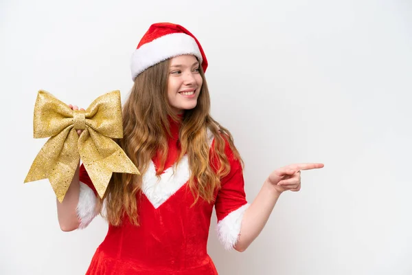 クリスマスのドレスを保持している若い白人女性クリスマスの弓は 製品を提示する側を指している白い背景に隔離 — ストック写真