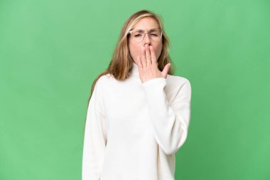 İzole edilmiş arka planda genç sarışın kadın esniyor ve elleriyle ağzını kapatıyor.