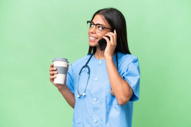 Genç Afrikalı Amerikalı hemşire, izole edilmiş arka planda kahve ve cep telefonu tutuyor.