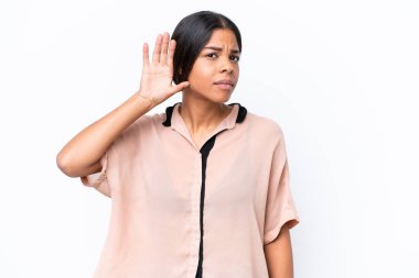 Genç Afrikalı Amerikalı bir kadın beyaz arka planda izole edilmiş bir şekilde elini kulağına koyarak bir şeyler dinliyor.