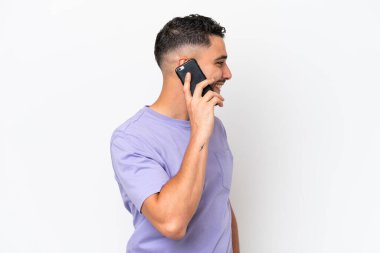 Beyaz arka planda izole edilmiş genç Arap yakışıklı bir adam cep telefonuyla sohbet ediyor.