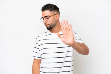 Beyaz arka planda izole edilmiş genç Arap yakışıklı adam dur hareketi yapıyor ve hayal kırıklığına uğruyor.