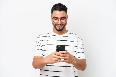 Genç Arap yakışıklı adam beyaz arka planda izole edilmiş cep telefonuyla bir mesaj gönderiyor.