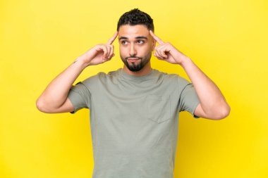 Genç Arap yakışıklı adam sarı arka planda izole edilmiş. Şüpheleri ve düşünceleri var.