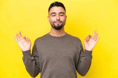 Sarı arka planda, Zen pozisyonunda, yakışıklı genç bir Arap.