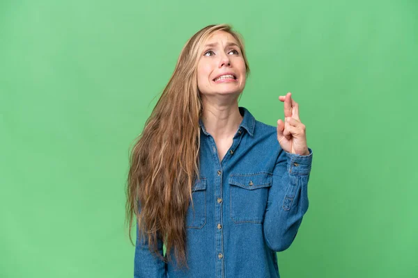 Young blonde woman over isolated background with fingers crossing and wishing the best