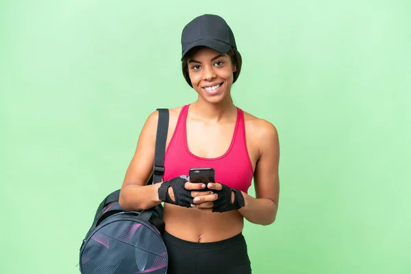 Young sport African american woman with sport bag over isolated background sending a message with the mobile