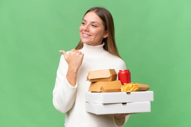 Sarışın, güzel bir kadın, yiyecekleri izole edilmiş arka planda tutuyor. Ürünü sunmak için yan tarafa bakıyor.