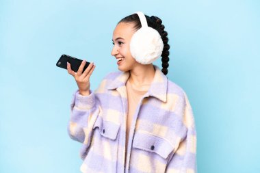 Mavi arka planda izole edilmiş kışlık kuklalar takan genç bir Arap kadın cep telefonuyla sohbet ediyor.