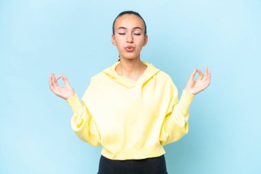 Genç Arap kadın, mavi arka planda Zen pozuyla izole edilmiş.