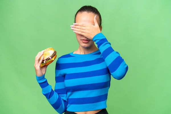 Młoda Arabka Trzymająca Hamburgera Nad Odosobnionym Tłem Zakrywającym Oczy Dłońmi — Zdjęcie stockowe